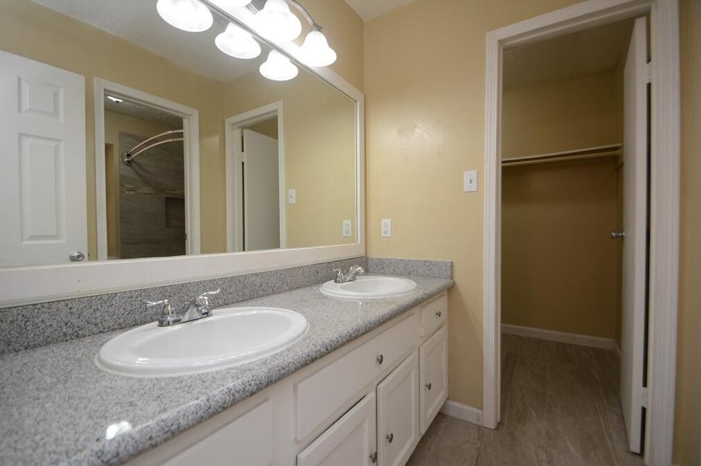 15 South Tallowberry Drive Spring, TX 77381 - Photo 18 of 26 Bathroom with double vanity, granite countertops, ample storage, large mirror, and an adjacent walk-in closet with neutral finishes.