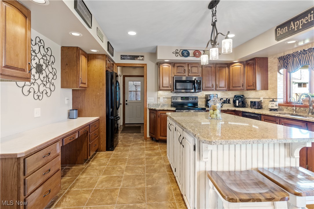 7285 South Raccoon Road Canfield, OH 44406 - Photo 6 of 46 Kitchen with appliances with stainless steel finishes, a sink, tasteful backsplash, a center island, and light stone counters