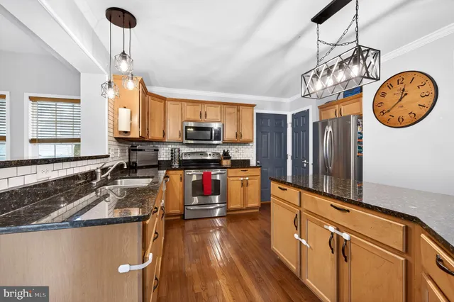 a open kitchen with stainless steel appliances granite countertop a stove top oven a sink a dining table and chairs with wooden floor