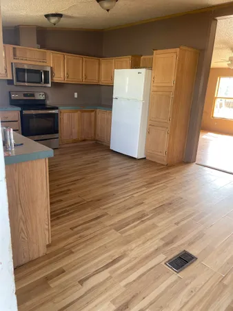 an empty room with wooden floor and kitchen view
