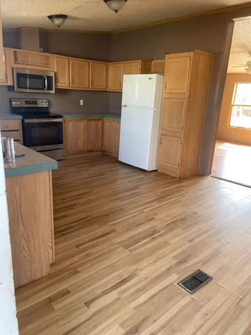 an empty room with wooden floor and kitchen view