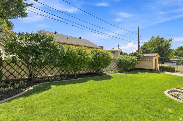 702 North 150 West Logan, UT 84321 - Photo 42 of 51 Expansive green lawn with a decorative lattice fence, mature shrubs, a defined garden bed, and an exterior storage shed
