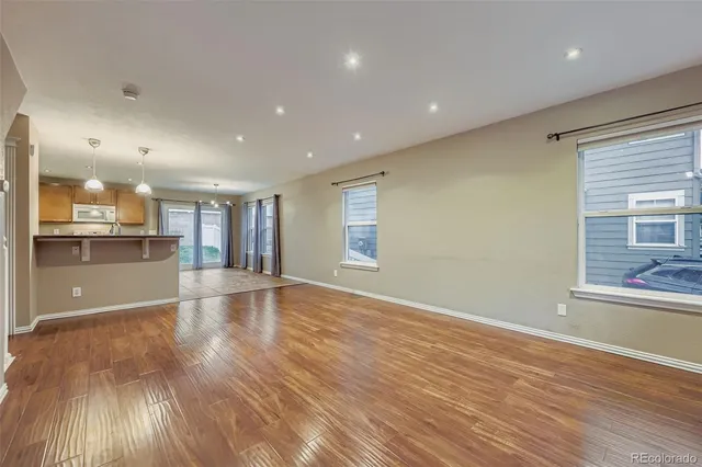 a view of empty room with wooden floor and kitchen view