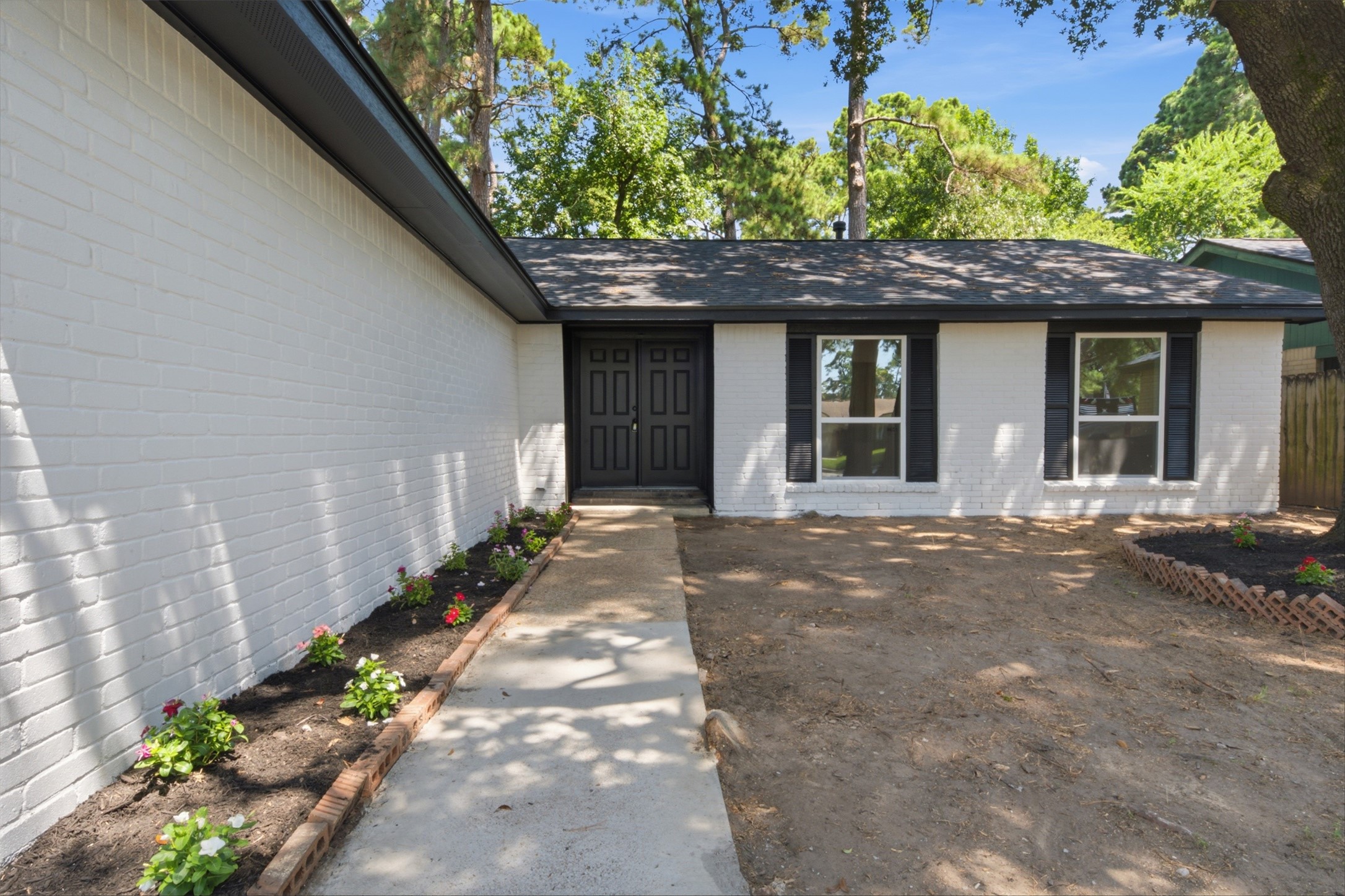 9518 Landry Boulevard Spring, TX 77379 - Photo 3 of 38 Charming single-story home with a fresh white brick exterior, accented by black shutters and a welcoming front walkway bordered by vibrant flower beds.