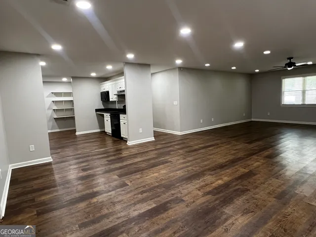 an empty room with wooden floor and a kitchen
