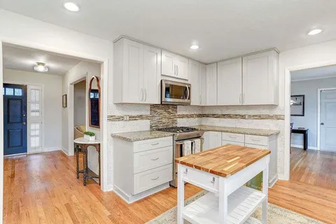 a kitchen with granite countertop a stove top oven a sink dishwasher and a refrigerator with wooden floor