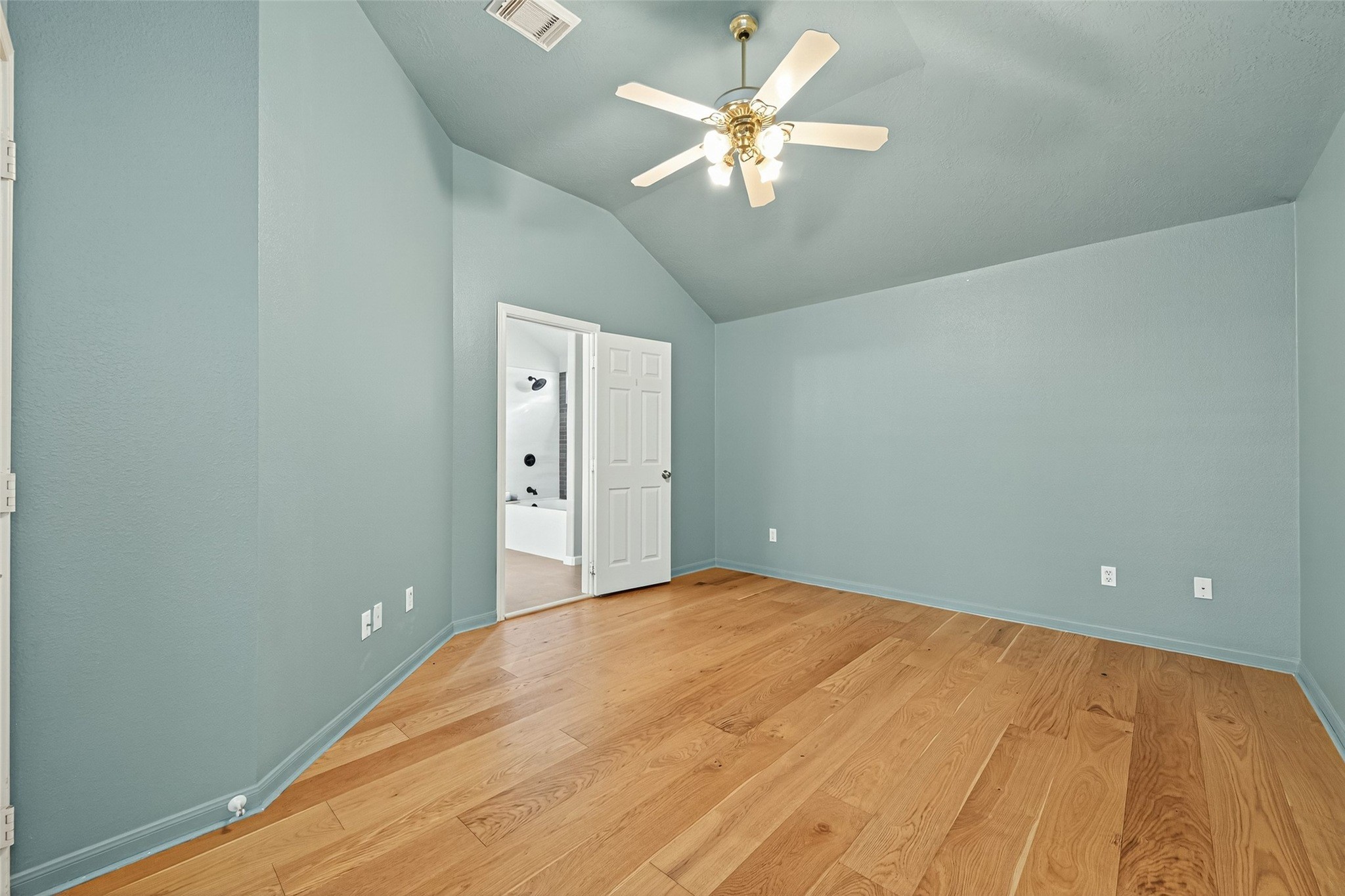 2910 Crescent Bend Road Spring, TX 77388 - Photo 13 of 29 This room features light blue walls, a vaulted ceiling with a ceiling fan, and warm wood flooring. It has a doorway leading to a bathroom.