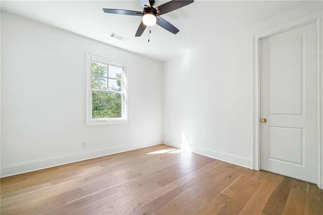 an empty room with wooden floor fan and windows