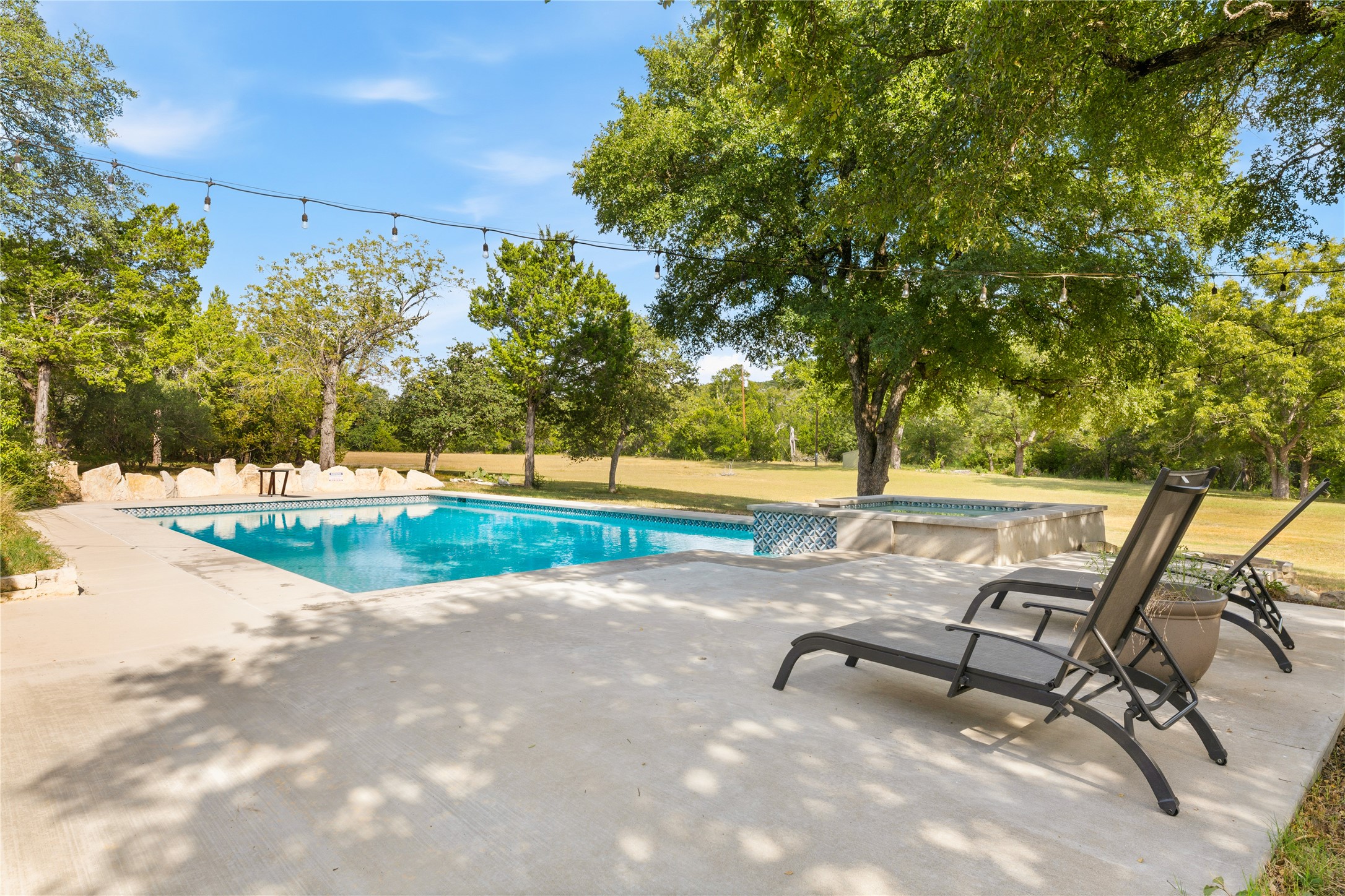 12901 Wire Road Leander, TX 78641 - Photo 23 of 40 Mature trees frame a sparkling swimming pool and concrete patio under open skies.