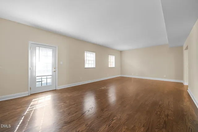 a view of an empty room with wooden floor and window
