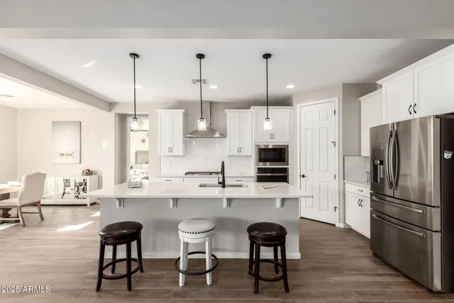 a room with stainless steel appliances kitchen island granite countertop a dining table chairs refrigerator and sink