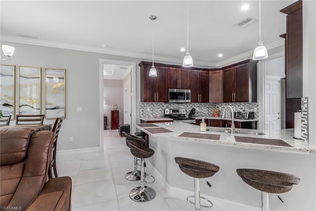 4143 2nd Avenue Northeast Naples, FL 34120 - Photo 7 of 15 a kitchen with stainless steel appliances granite countertop a stove a sink a refrigerator white cabinets and couches with wooden floor