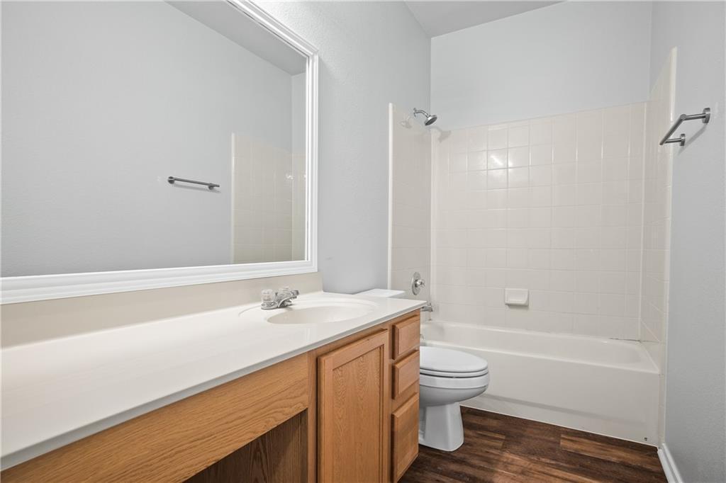 19909 Sap Cove Round Rock, TX 78664 - Photo 12 of 22 Bathroom featuring a wood-finish vanity with a single basin sink and light-toned countertop, a full-width mirror, and a shower-over-tub combination with white subway tile surround