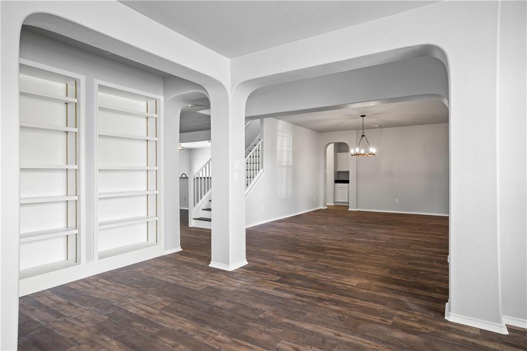 19909 Sap Cove Round Rock, TX 78664 - Photo 4 of 22 Spacious living area featuring wood-finish flooring, built-in shelving, arched doorways, a modern chandelier, and a white staircase with dark treads