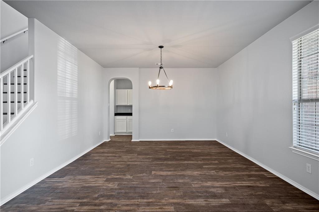 19909 Sap Cove Round Rock, TX 78664 - Photo 5 of 22 Spacious interior featuring wood-finish flooring, a contemporary chandelier, and an arched doorway leading to a kitchen with white cabinetry