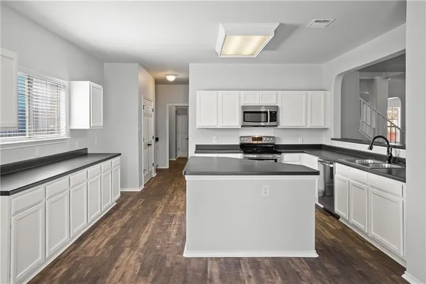 a kitchen with stainless steel appliances a stove top oven a sink a refrigerator white cabinets and wooden floor