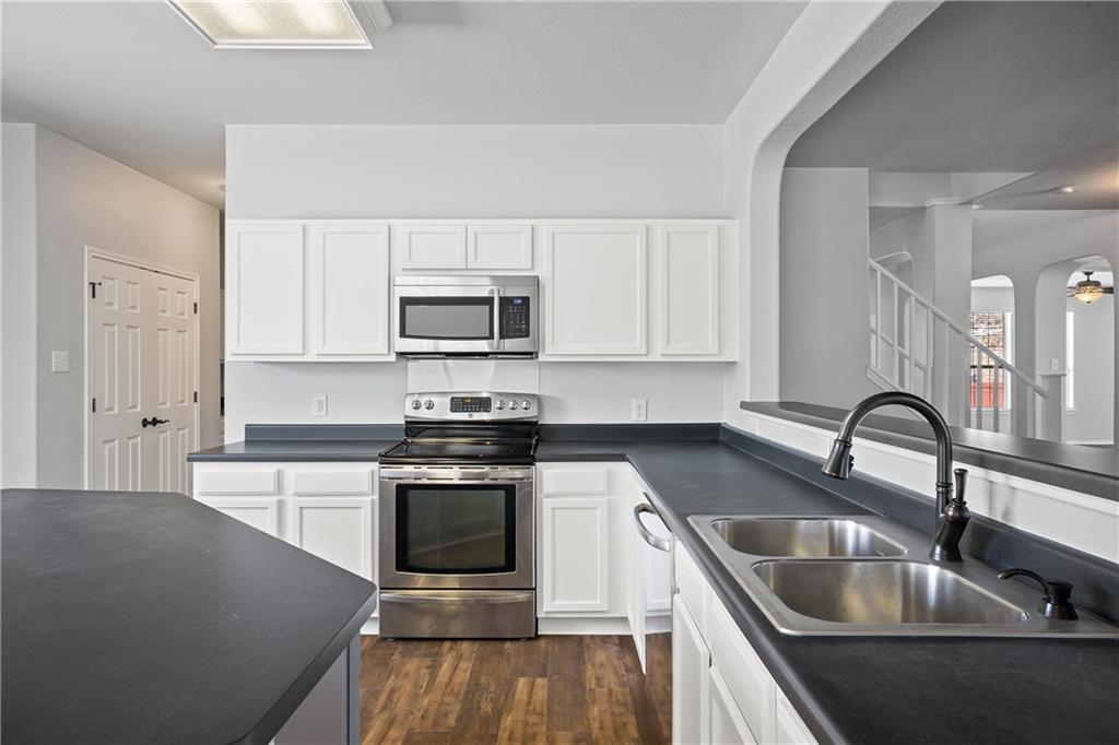 19909 Sap Cove Round Rock, TX 78664 - Photo 9 of 22 Kitchen featuring white cabinetry, dark countertops, wood-finish flooring, stainless steel appliances, and a double basin sink with a gooseneck faucet