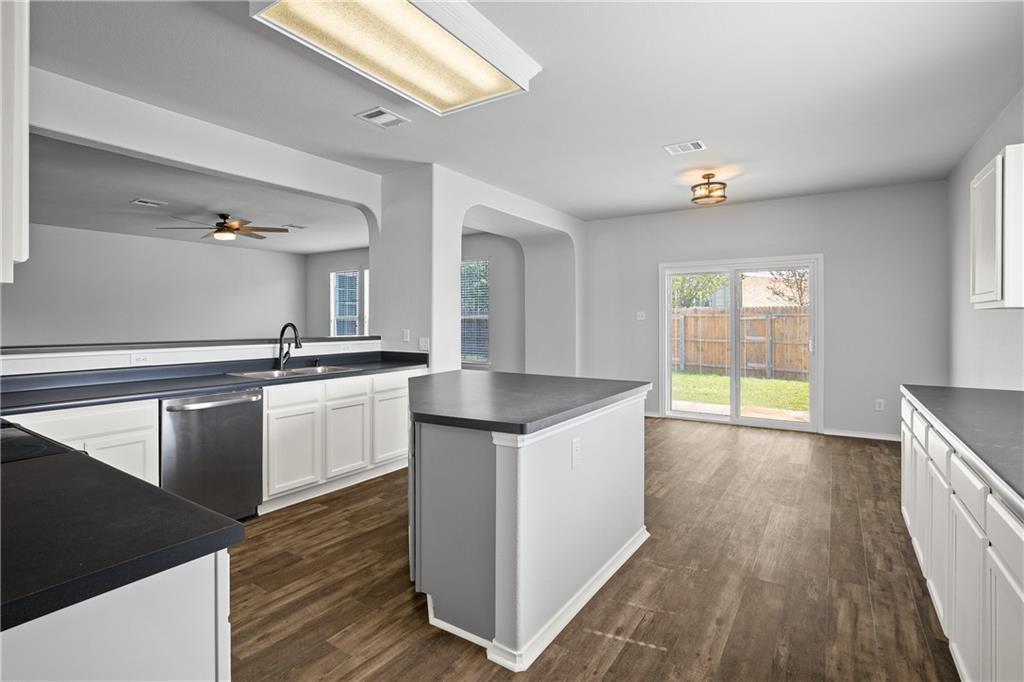 19909 Sap Cove Round Rock, TX 78664 - Photo 10 of 22 Kitchen and dining area featuring dark countertops, white cabinetry, stainless steel dishwasher, wood-finish flooring, and sliding glass doors to the backyard