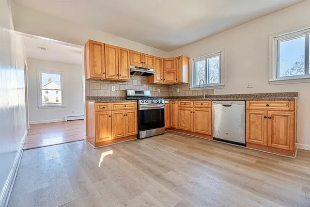 a large kitchen with stainless steel appliances granite countertop a stove top oven a sink dishwasher and white cabinets with wooden floor