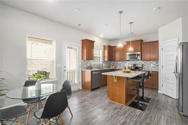 a kitchen with stainless steel appliances granite countertop a stove a sink a refrigerator and a dining table with wooden floor