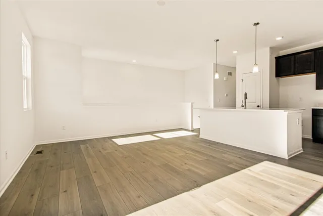 a view of an empty room with wooden floor and a kitchen