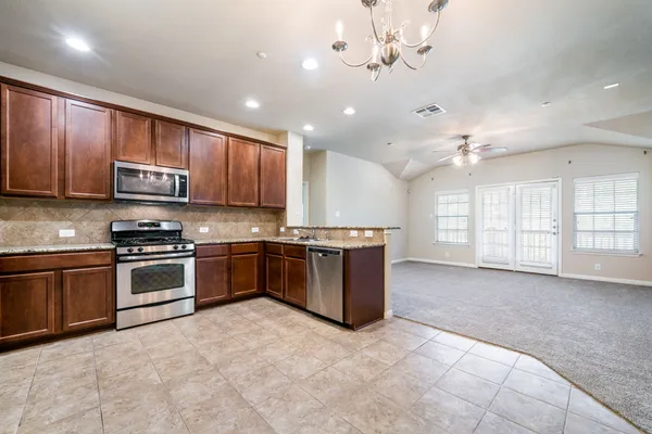 a large kitchen with stainless steel appliances granite countertop a stove a sink dishwasher a microwave oven and a refrigerator with wooden cabinets