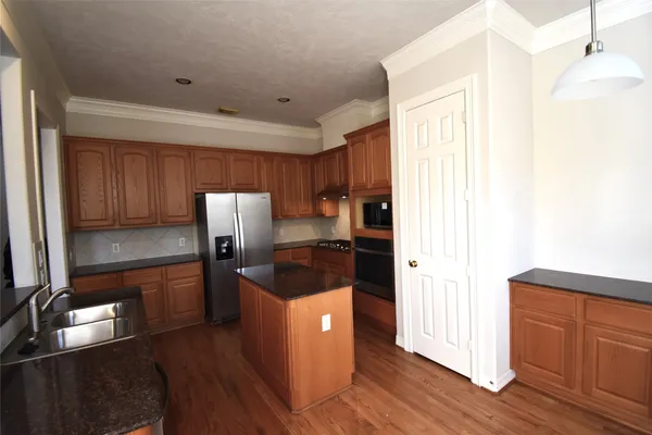 a kitchen with granite countertop a refrigerator a sink dishwasher and wooden cabinets with wooden floor