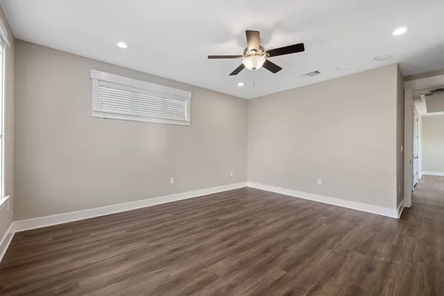 a view of an empty room with wooden floor and a ceiling fan