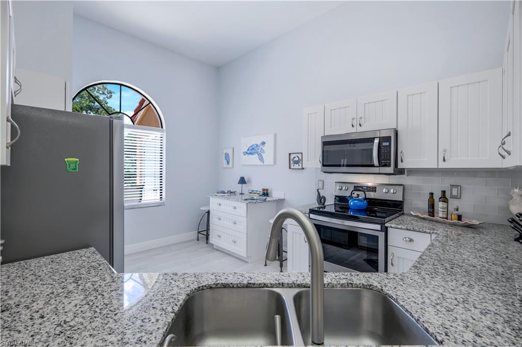 637 Beachwalk Circle, Unit E203 Naples, FL 34108 - Photo 7 of 30 a kitchen with stainless steel appliances granite countertop a sink a stove a microwave a dining table and chair