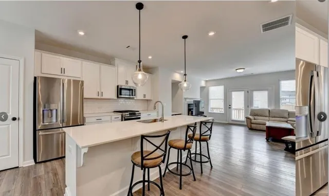 a kitchen with stainless steel appliances kitchen island granite countertop a refrigerator a stove a sink with island chairs and wooden floor