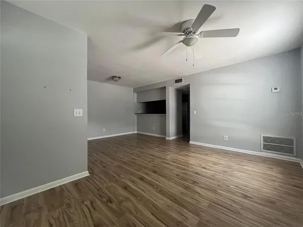 an empty room with wooden floor ceiling fan and windows