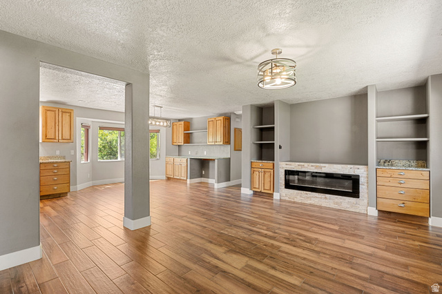 55 Spring Drive Toquerville, UT 84774 - Photo 8 of 36 Unfurnished living room featuring a textured ceiling, light wood finished floors, a stone fireplace, and built in features