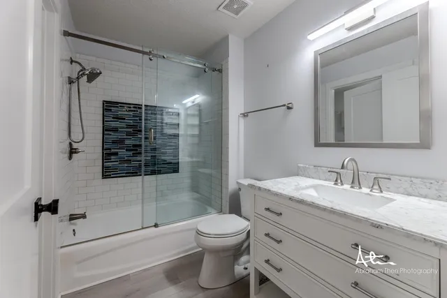 a bathroom with a granite countertop toilet a sink a mirror a shower and vanity