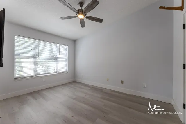 an empty room with wooden floor fan and windows