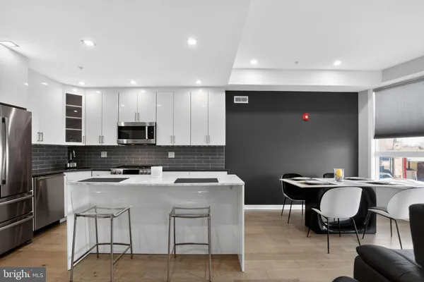 a kitchen with stainless steel appliances granite countertop a stove a sink a microwave a refrigerator and chairs