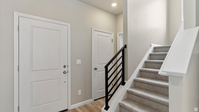 82 Provo River Road, Unit 251 Saratoga Springs, UT 84045 - Photo 2 of 32 Entryway featuring a white paneled door, wood-finish flooring, and a carpeted staircase with a modern black iron railing