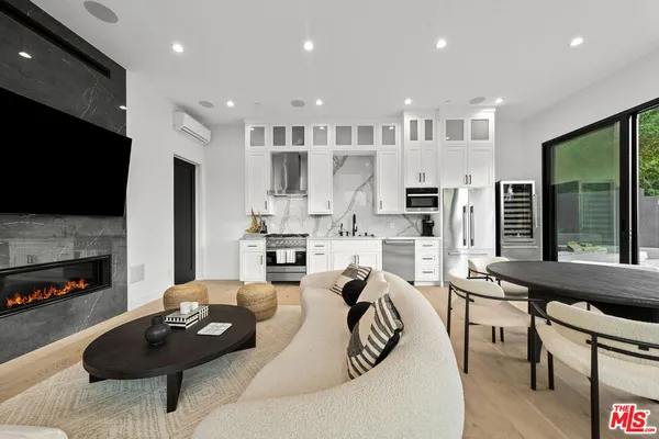 a living room with stainless steel appliances furniture a flat screen tv and a large window