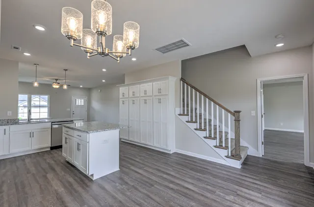 a open kitchen with stainless steel appliances granite countertop a refrigerator a stove top oven a sink dishwasher and white cabinets with wooden floor