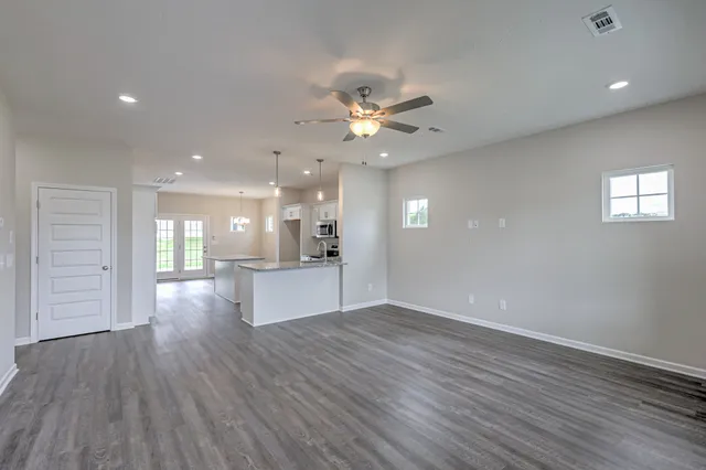 a view of an empty room and kitchen with wooden floor