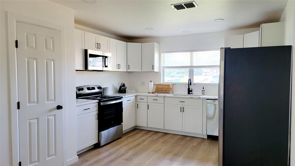 1447 West Lingleville Road Stephenville, TX 76401 - Photo 6 of 12 Kitchen featuring appliances with stainless steel finishes, light countertops, light wood-type flooring, and white cabinetry