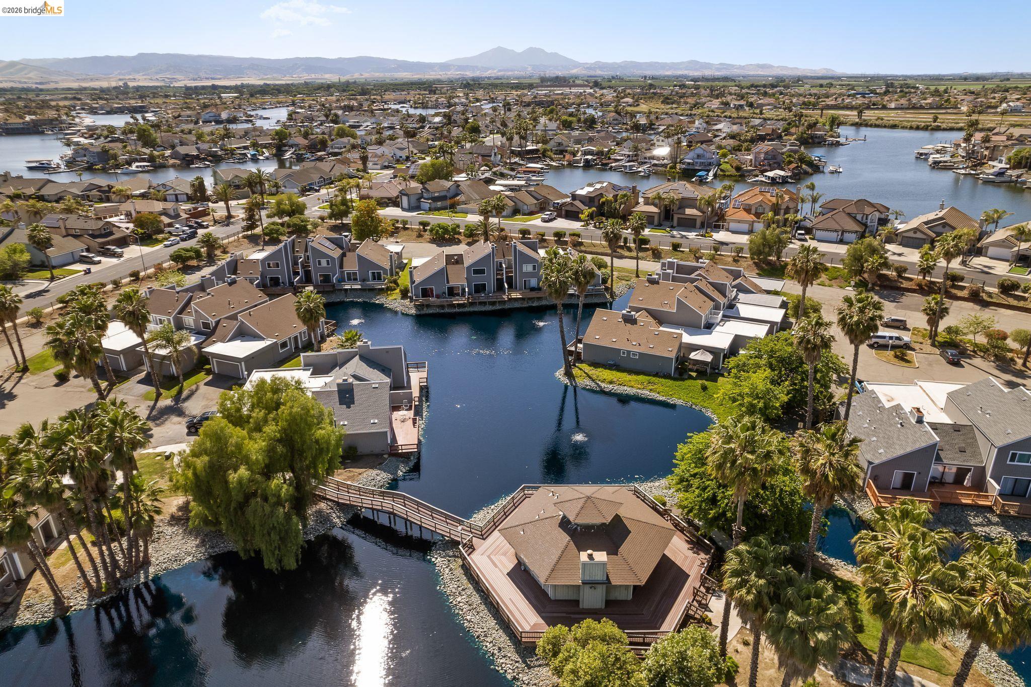 Lakeside community featuring waterfront homes, extensive palm tree landscaping, a central octagonal pavilion, and a pedestrian bridge