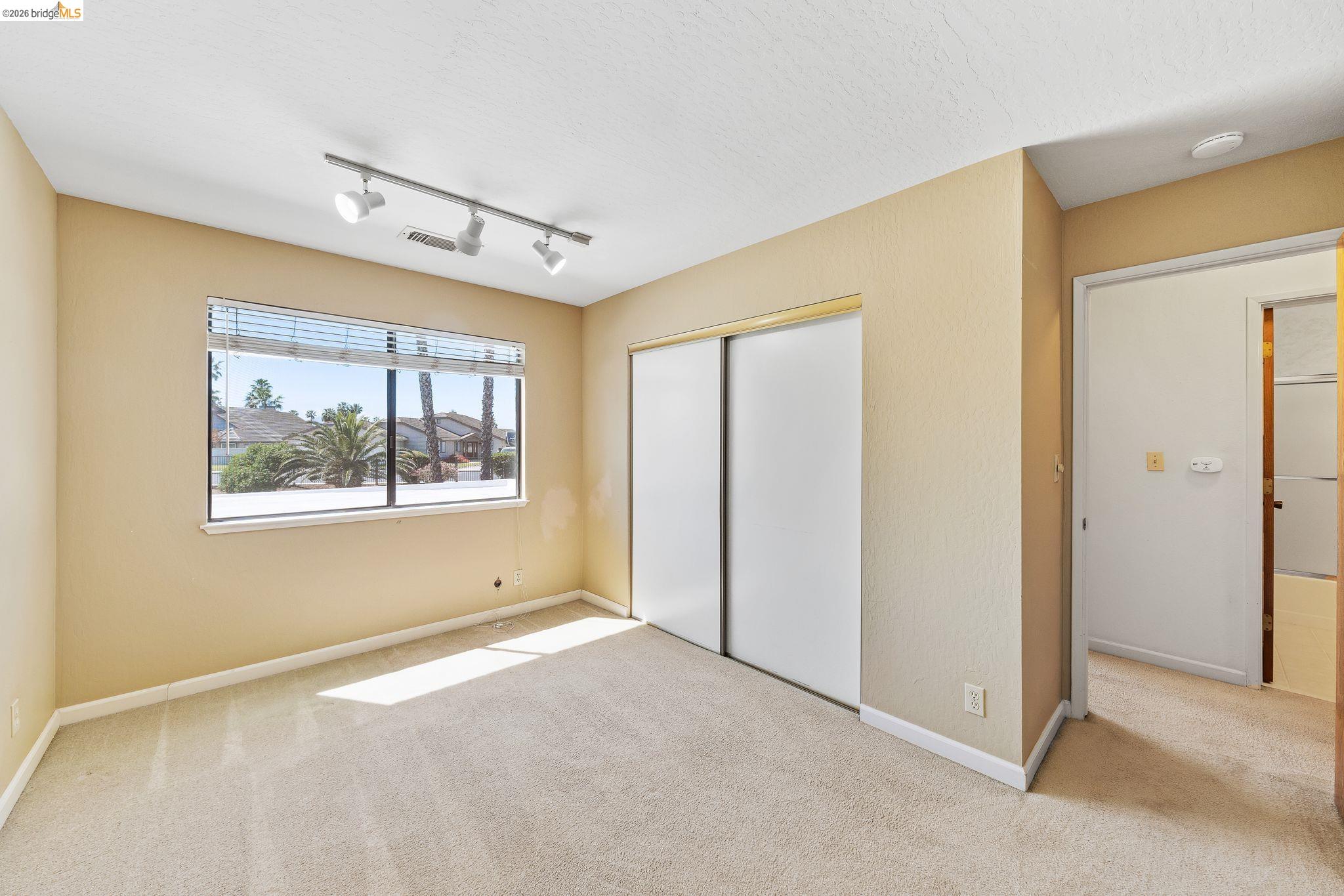 2051 Sand Point Road Discovery Bay, CA 94505 - Photo 32 of 47 Carpeted room featuring a large window with horizontal blinds, a sliding door closet, and track lighting