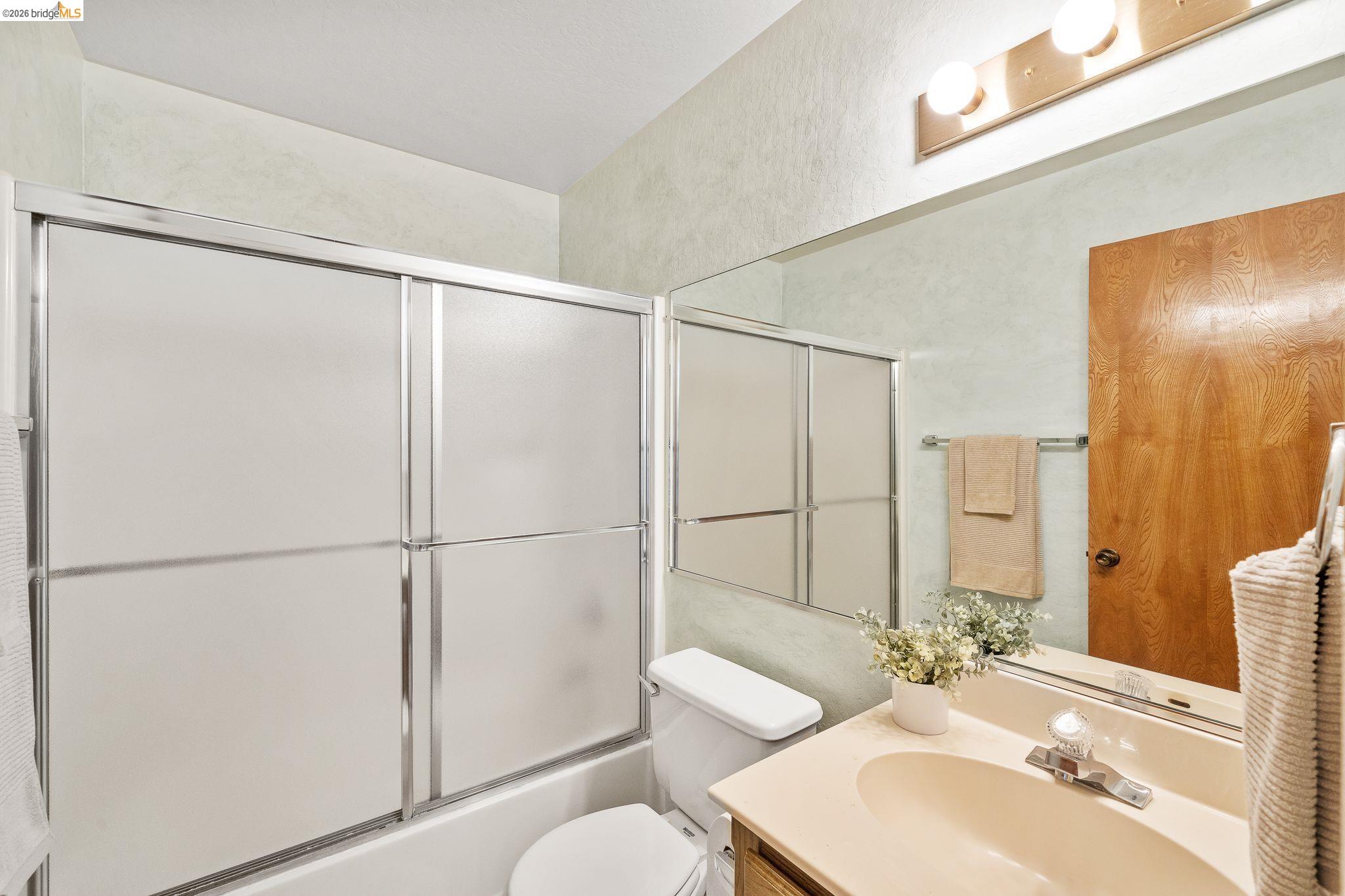 2051 Sand Point Road Discovery Bay, CA 94505 - Photo 34 of 47 Bathroom featuring a shower/tub combination with sliding frosted glass doors, a vanity with an integrated sink, a large wall-mounted mirror, and overhead strip lighting