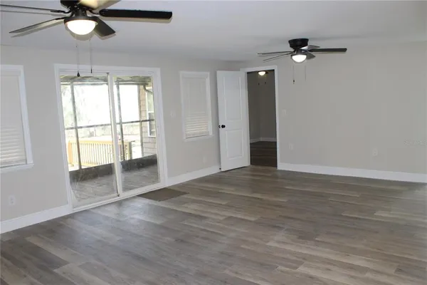 an empty room with wooden floor fan and windows