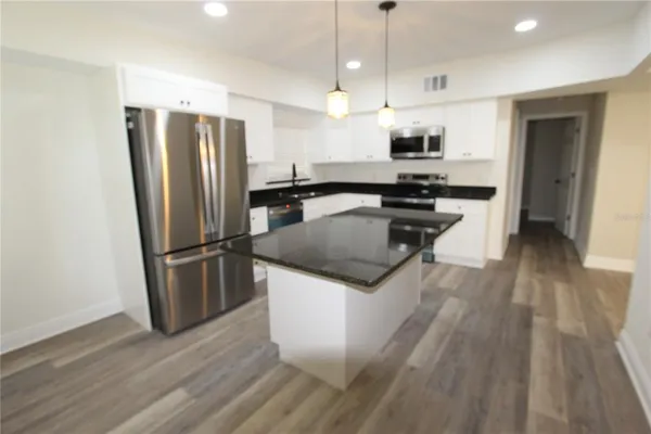 a kitchen with stainless steel appliances granite countertop a refrigerator a stove a sink and a wooden floor