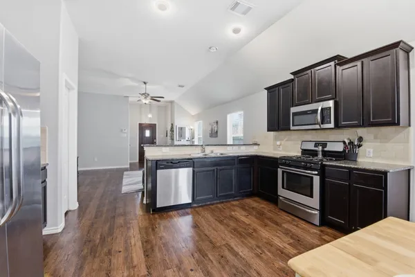 a kitchen with stainless steel appliances kitchen island granite countertop a stove a sink dishwasher and a microwave oven with wooden floor