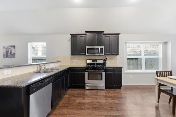 a kitchen with granite countertop a stove top oven a sink dishwasher a dining table and chairs