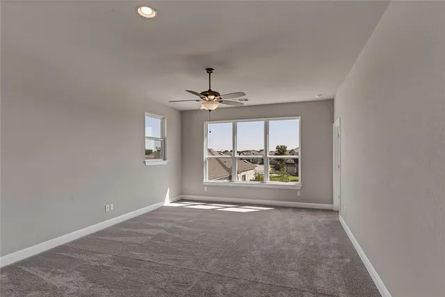 an empty room with chandelier fan and windows