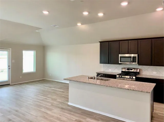 a kitchen with granite countertop a sink a stove a microwave a counter top space and cabinets