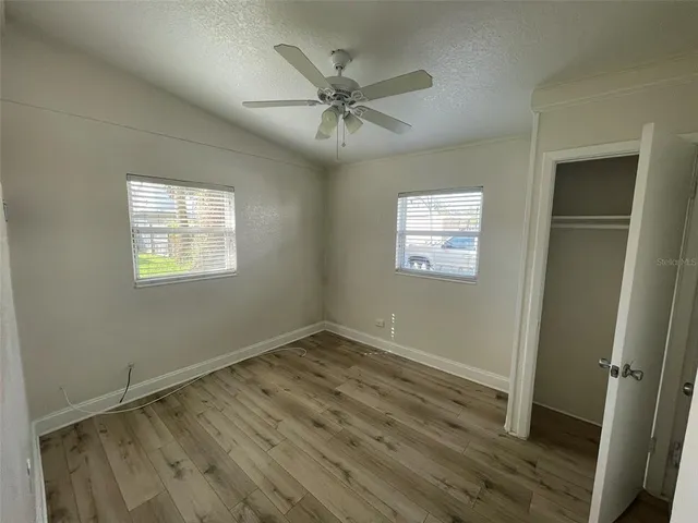 an empty room with wooden floor fan and windows